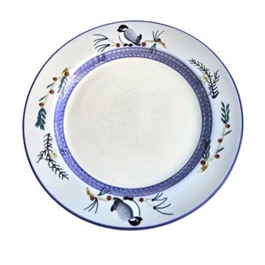 Puede incluir: Plato de cerámica blanco con borde azul y borde decorativo. El borde presenta un diseño azul y blanco con pájaros pintados y ramitas de vegetación y bayas. El plato tiene un centro blanco.