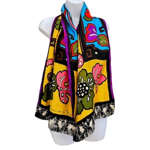 May include: A vibrant scarf featuring a bold floral pattern in yellow, bright blue, pink, and olive green. The design includes black geometric borders, purple trim, and a bottom edge with a black and white tassel print. Oscar de la Renta is signed.