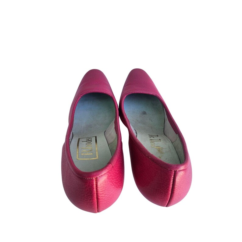 May include: A pair of bright pink leather flats. The shoes have a pointed toe and a low heel. The interior of the shoe is a light blue color with gold lettering that reads "Rhodes". The shoes are set against a white background.