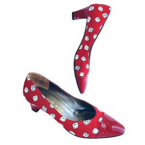 May include: Red heels with a repeating white and black letter design. The heels have a patent leather toe and heel. The brand name "BRUNO MAGLI" is visible on the insole.