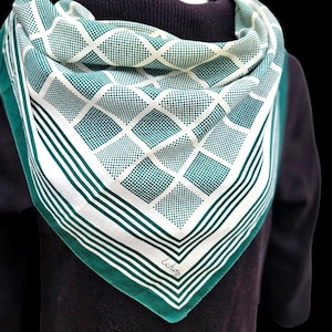 May include: A square scarf with a geometric pattern in white and teal green. The scarf features a diamond and dot design, with a solid green border and striped accents. The brand name "Echo" is visible in the corner. The scarf is draped over a dark-colored garment.
