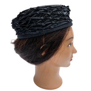 May include: A black hat with a woven, openwork design. The hat has a structured shape with a brim and a textured crown. The hat is displayed on a mannequin head.