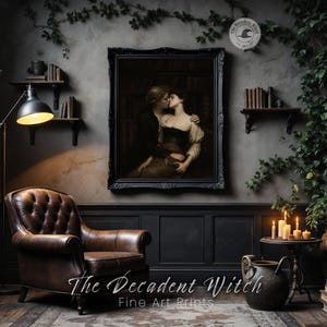 May include: A framed print of a couple embracing, hanging above a brown leather armchair. The room is decorated in dark tones with a floor lamp, shelves with books, and a small table with candles. The text "The Decadent Witch Fine Art Prints" is at the bottom.