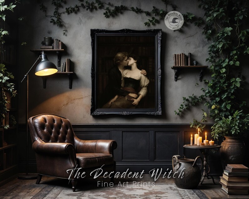 May include: A framed print of a couple embracing, hanging above a brown leather armchair. The room is decorated in dark tones with a floor lamp, shelves with books, and a small table with candles. The text "The Decadent Witch Fine Art Prints" is at the bottom.
