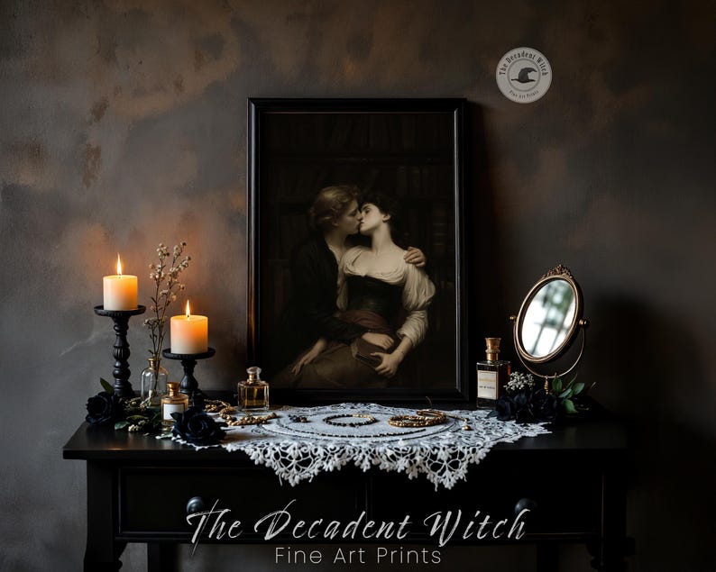 May include: A black table displays a framed artwork of a couple kissing, flanked by lit candles in black holders, perfume bottles, and a small mirror. A white lace doily and jewelry adorn the table. The text "The Decadent Witch Fine Art Prints" is visible.