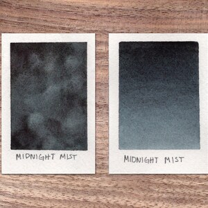 Könnte beinhalten: Zwei Aquarell-Farbmuster von Midnight Mist Tinte. Das erste Muster zeigt eine dunkle, wolkig und ungleichmäßige Anwendung der Tinte. Das zweite Muster zeigt einen glatten, gleichmäßigen Verlauf der Tinte von dunkel nach hell.