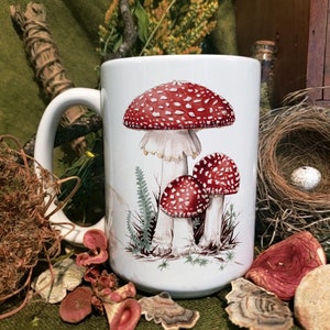 Puede incluir: Taza de cerámica blanca con un diseño de setas rojas y blancas. La taza tiene un asa grande y un fondo blanco. Las setas están representadas en un estilo realista con sombreros rojos y tallos blancos.