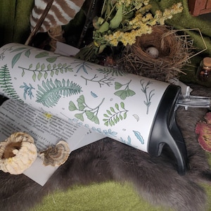 May include: White stainless steel water bottle with a green and blue floral design. The bottle has a black lid and a clear straw.