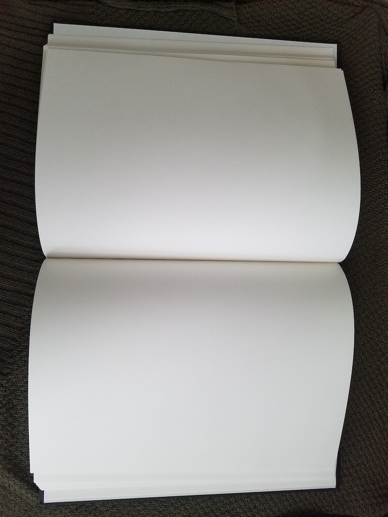 Puede incluir: Un libro blanco de tapa dura, en blanco, con lomo y p&aacute;ginas. El libro est&aacute; abierto y acostado sobre una superficie marr&oacute;n.