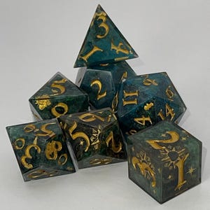May include: A collection of teal-coloured polyhedral dice with gold numerals and accents. The set includes various shapes, such as d4, d6, d8, d10, d12, and d20 dice. Ideal for tabletop role-playing games and other dice games.