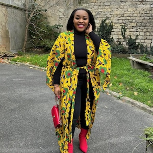 May include: A long yellow, green, and red patterned kimono with a black mock neck shirt and black jeans. The person is wearing red ankle boots.