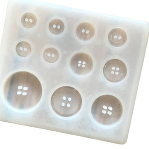 May include: A white silicone mould for making resin buttons. The mould has 12 different sized circles, each with a different number of holes for buttons.