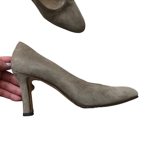 May include: A pair of light brown suede pumps with a high heel. The shoes have a pointed toe and a simple design.