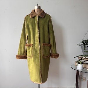 Peut inclure: Un long manteau vert olive avec une garniture en fausse fourrure marron sur le col, les poignets et les poches. Le manteau est présenté sur un mannequin. Le manteau a une esthétique vintage.
