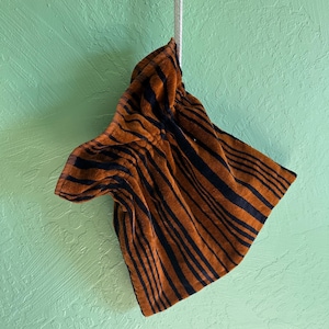 May include: A brown and black striped towel hanging from a white rope against a textured, light green wall. The towel has a tiger stripe pattern.