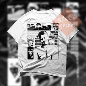 Puede incluir: Camiseta blanca con un diseño gráfico que presenta un retrato en blanco y negro, texto y otras ilustraciones. El texto incluye "FAKEMINK" y "Wild One". La camiseta tiene cuello redondo y mangas cortas.