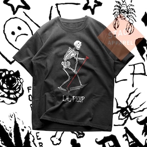 Puede incluir: Camiseta gris oscuro con un esqueleto blanco esquiando con un bastón rojo y una guadaña. El texto "LIL PEEP" está impreso debajo del gráfico. La camiseta es de STACK APPAREL.