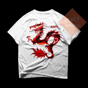 May include: White t-shirt featuring a red and black dragon design. The word "zushi" is printed in red on the shirt. The shirt is from Stacy Apparel.