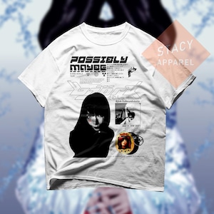 May include: White t-shirt with a graphic design including the text "POSSIBLY MAYBE" and the name "Bjork". The design incorporates a portrait and Japanese text. The shirt also features the text "STACY APPAREL".