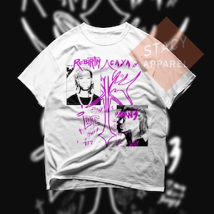 May include: White t-shirt with a graphic design featuring two black and white portraits and purple text. The text includes the words "Rebirth," "Acaya," and "DC." The shirt also has the text "Stacy Apparel."
