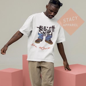 Puede incluir: Camiseta blanca con un gr&aacute;fico de las palabras "Elliott Smith" y una imagen de vaqueros y zapatos. Las palabras "Son of Sam" est&aacute;n escritas en rojo debajo. La camiseta es de Stacy Apparel.