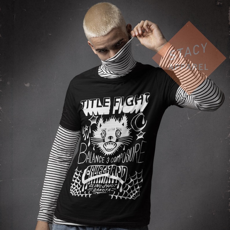 May include: Black t-shirt featuring a white cat graphic, the words "TITLE FIGHT", "BALANCE & COMPOSURE", and "CHUGGAARD". The t-shirt is layered over a striped long-sleeved top.