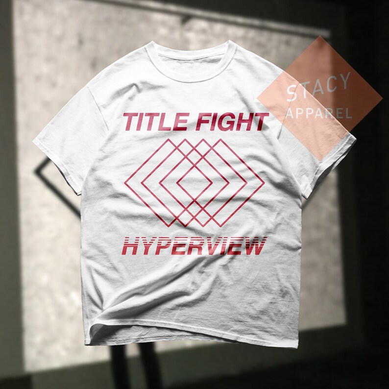 Puede incluir: Camiseta blanca con las palabras "TITLE FIGHT" y "HYPERVIEW" en rojo, junto con un dise&ntilde;o geom&eacute;trico rojo. La camiseta es de Stacy Apparel.