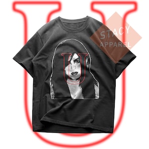 May include: A black short-sleeve t-shirt featuring a white graphic illustration of a person with long hair and a red letter U overlaid on the face. The text STACY APPAREL is printed in the upper right corner. A large red letter U is in the background.