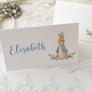 May include: White place card with a blue and brown illustration of Peter Rabbit. The name "Elizabeth" is written in blue cursive.