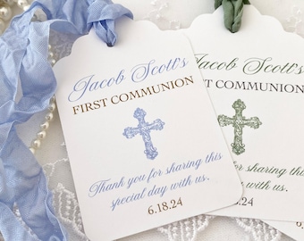 May include: Two white favor tags with scalloped edges. The top tag has blue text that reads "Jacob Scott's First Communion" and a blue cross. The bottom tag has green text that reads "Jacob Scott's First Communion" and a green cross. Both tags have the text "Thank you for sharing this special day with us." and a date.