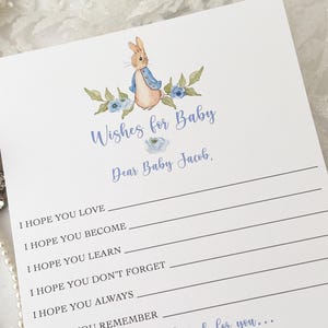 May include: A white card with blue and green floral accents and a watercolor illustration of Peter Rabbit. The card has the text "Wishes for Baby Dear Baby Jacob." and lines for writing wishes.