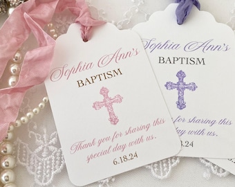 May include: Two white favor tags with scalloped edges. The top tag has pink text that reads "Sophia Ann's Baptism" with a pink cross. The bottom tag has purple text that reads "Sophia Ann's Baptism" with a purple cross. Both tags have a thank you message.