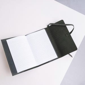 May include: A black leather-bound journal with a ribbon closure and lined pages. The journal is open to reveal the blank pages.