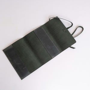 May include: A dark green leather roll-up case with a strap and a flap closure. The case is open and empty.