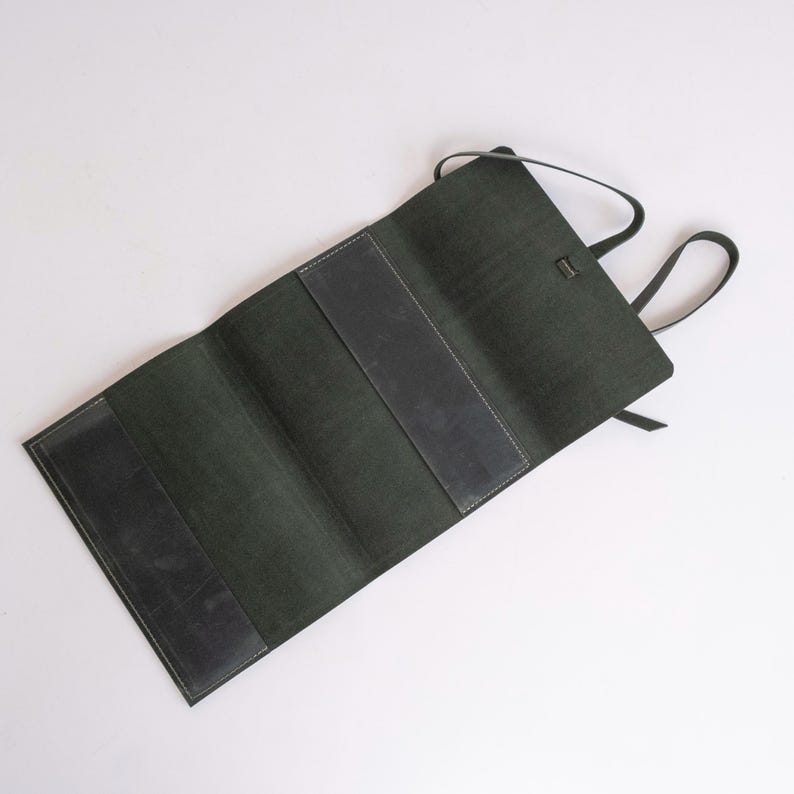 May include: A dark green leather roll-up case with a strap and a flap closure. The case is open and empty.