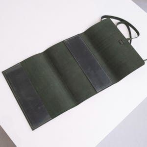 May include: A dark green leather roll-up case with three compartments. The case is folded open and the interior is lined with a dark gray fabric.