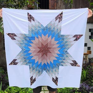 May include: A white quilt with a large blue and brown star pattern. The star is made up of smaller fabric squares in various shades of blue, brown, and pink.