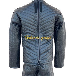 Puede incluir: Chaqueta y pantal&oacute;n acolchados negros con una cremallera en la parte delantera. La chaqueta tiene una cremallera negra y una tira de velcro negra en el cuello. El texto "Galactic Props" est&aacute; bordado en dorado en la chaqueta.