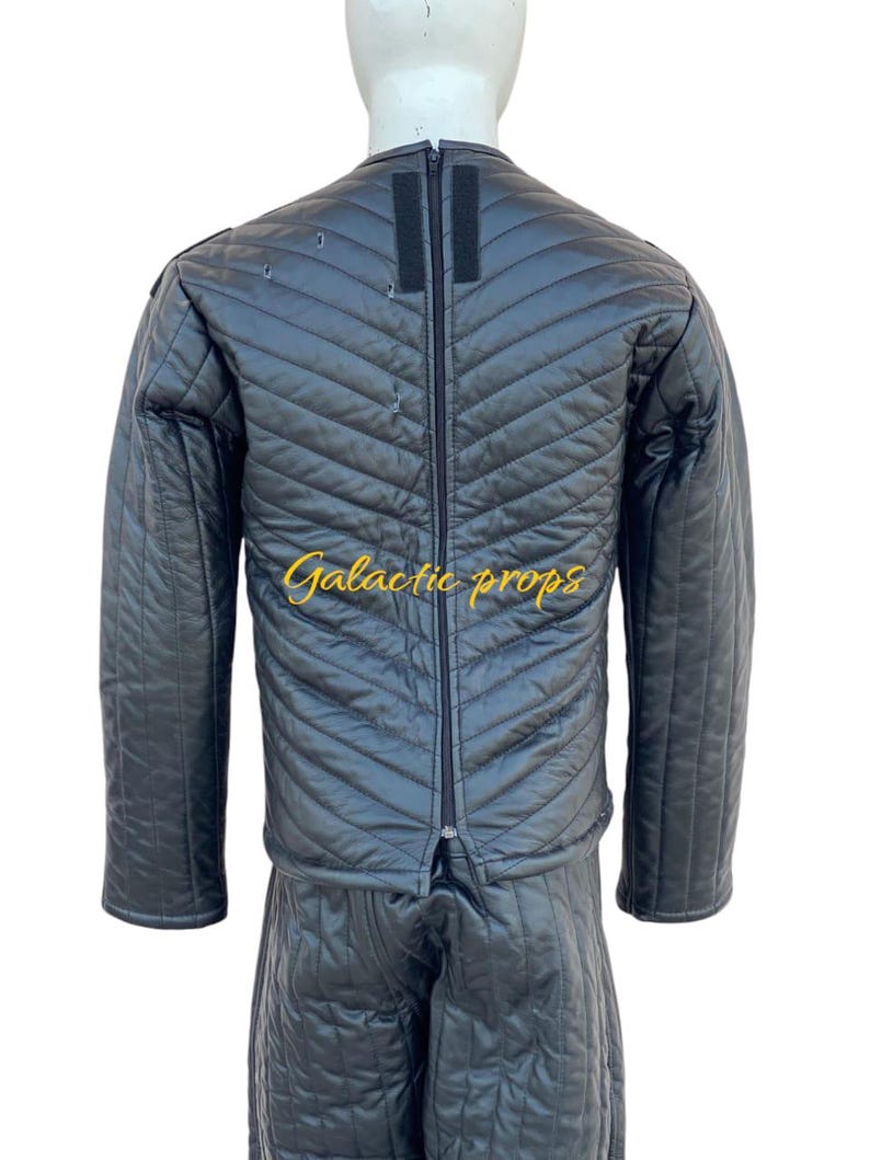 Puede incluir: Chaqueta y pantal&oacute;n acolchados negros con una cremallera en la parte delantera. La chaqueta tiene una cremallera negra y una tira de velcro negra en el cuello. El texto "Galactic Props" est&aacute; bordado en dorado en la chaqueta.