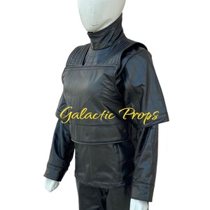 May include: Black costume with a high collar and quilted detailing. The costume includes a jacket with shoulder pads, a vest, and pants. The text "Galactic Props" is printed on the vest. The costume is displayed on a mannequin.