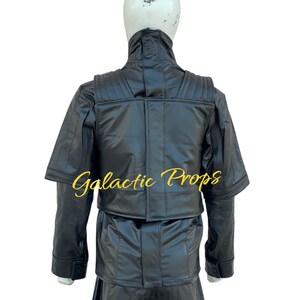 May include: Black costume with a high collar and quilted shoulder details. The costume includes a jacket and pants. The text "Galactic Props" is printed in gold script on the jacket. The costume is displayed on a mannequin.