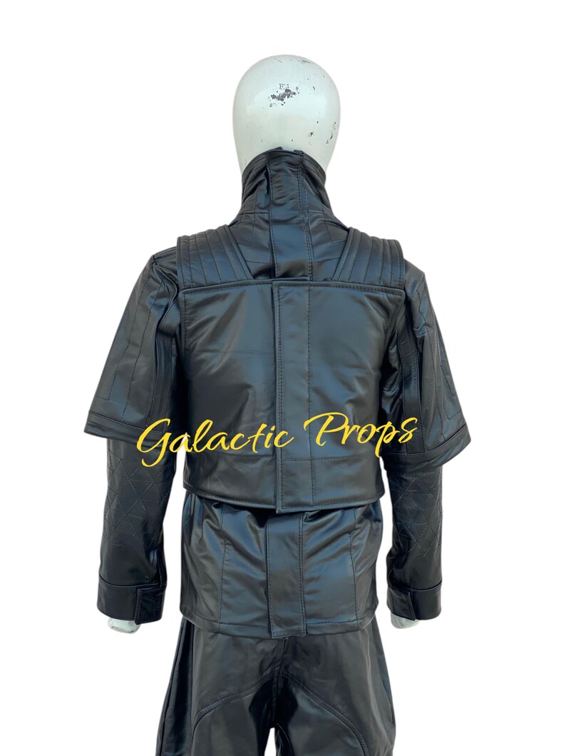 May include: Black costume with a high collar and quilted shoulder details. The costume includes a jacket and pants. The text "Galactic Props" is printed in gold script on the jacket. The costume is displayed on a mannequin.