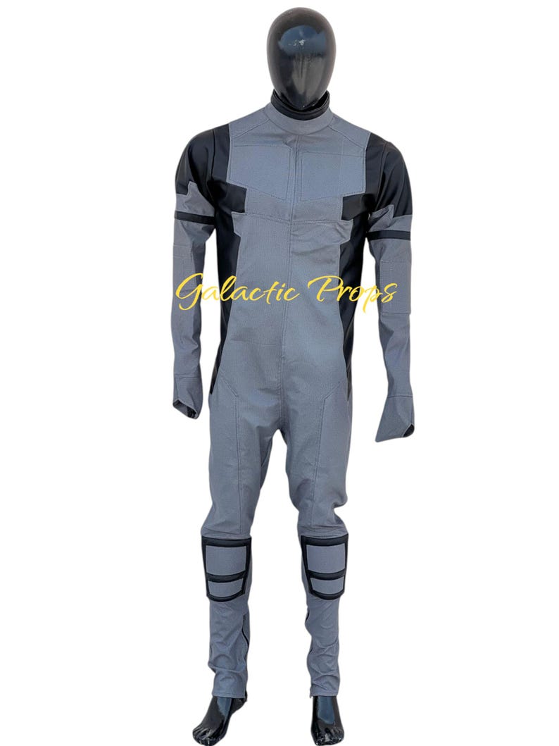 May include: Gray and black jumpsuit with a high collar and long sleeves. The jumpsuit has black accents on the shoulders, knees, and sleeves. The text "Galactic Props" is printed on the front.