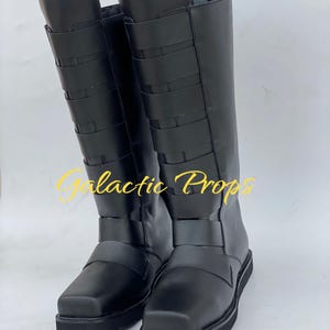 May include: A pair of black knee-high boots with multiple horizontal straps and a square toe. The boots have a flat sole and a zipper on the side. The text "Galactic Props" is visible in the image.