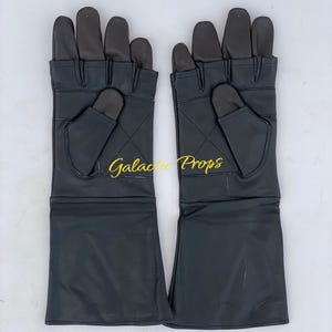 May include: A pair of black leather gloves with extended cuffs. The gloves have a dark grey palm and finger area, with a diamond pattern stitched on the back of the hand. The text "Galactic Props" is visible in gold script.