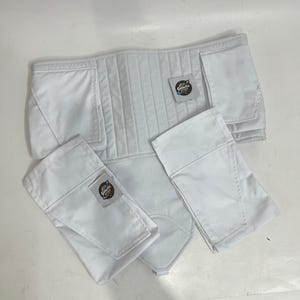 以下が含まれることがあります： 白いパッド入りのコスチュームパーツ。垂直ステッチとポケットが付いた幅広のベルトと、いくつかの長方形のパーツが含まれています。各パーツには、円形のデザインで「Galactic Props」というテキストが入った小さなタグが付いています。