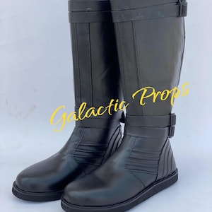 May include: Two black knee-high boots with buckle straps. The boots have a smooth, glossy finish and a flat sole. The text "Galactic Props" is written in yellow cursive across the image.