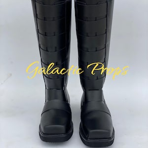 May include: A pair of black knee-high boots with a square toe and multiple horizontal straps. The boots have a tall shaft and a flat sole. The text "Galactic Props" is in yellow across the front of the boots.