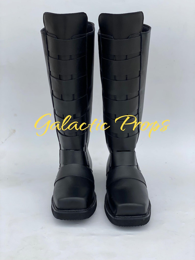 May include: A pair of black knee-high boots with a square toe and multiple horizontal straps. The boots have a tall shaft and a flat sole. The text "Galactic Props" is in yellow across the front of the boots.