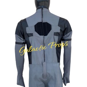 May include: A gray and black jumpsuit with a textured pattern, featuring a central zipper and black accents on the shoulders and chest. The back view of the costume is displayed on a mannequin. The text "Galactic Props" is visible.